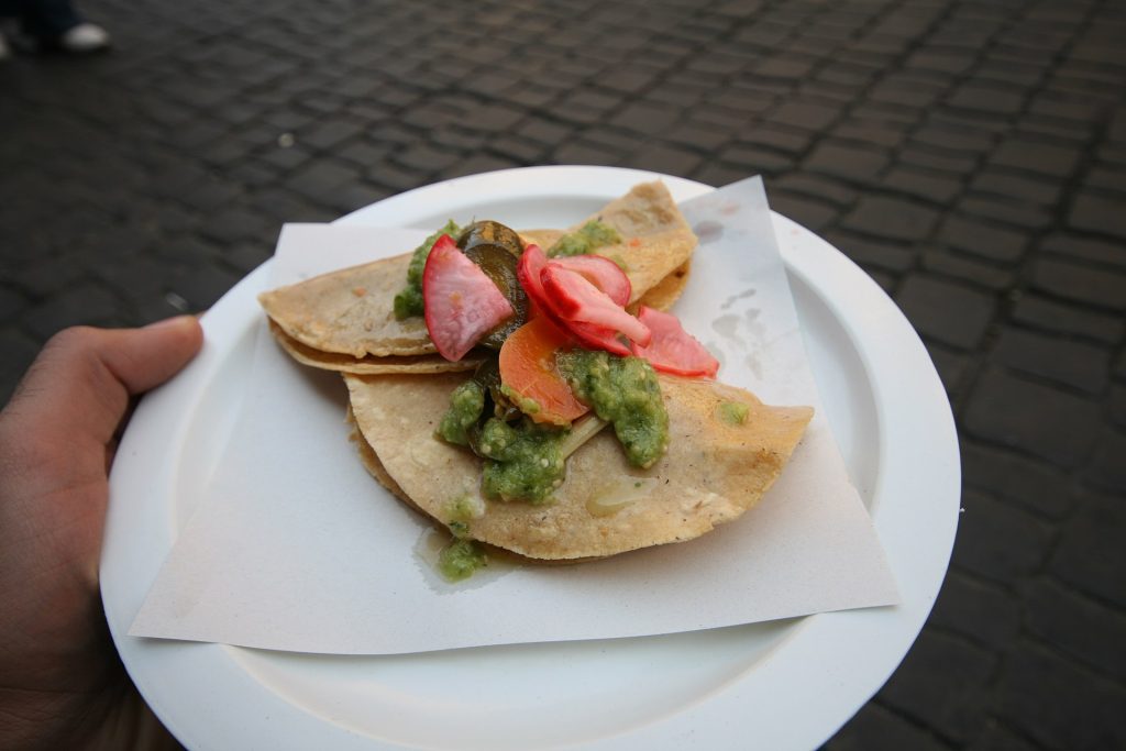 A paper plate of street tacos topped with onion and coriander